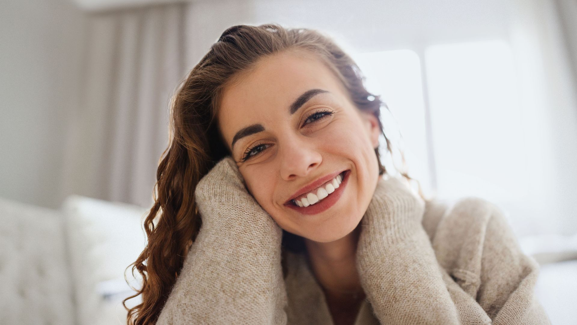 Mujer sonriendo con un suéter acogedor y un fondo desenfocado.